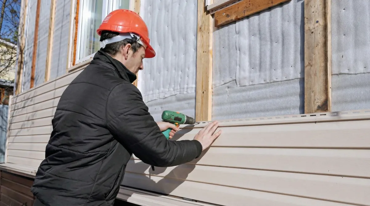 Siding replacement professional using a power drill to install new tan vinyl siding on a home exterior in Arvada, CO